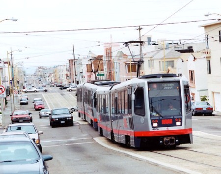 N-Judah Line Muni Metro light rail transit (LRT) train running in raised median on San Francisco's Judah St. Alignment in this constricted 80-foot-wide arterial includes space for 2 dedicated light rail tracks, 4 vehicle lanes, and shared sidewalk for pedestrians and bicyclists. Similar alignment design could fit dedicated LRT tracks, 4 traffic lanes, and sidewalks into Austin's Guadalupe-Lamar corridor. Photo (copyright) Eric Haas.