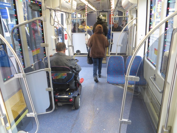 Passenger in wheelchair easily maneuvers chair into accessible space aboard car. In contrast to buses — no tiedowns, no operator assistance needed, no passengers ousted from their seats!  Photo: L. Henry.